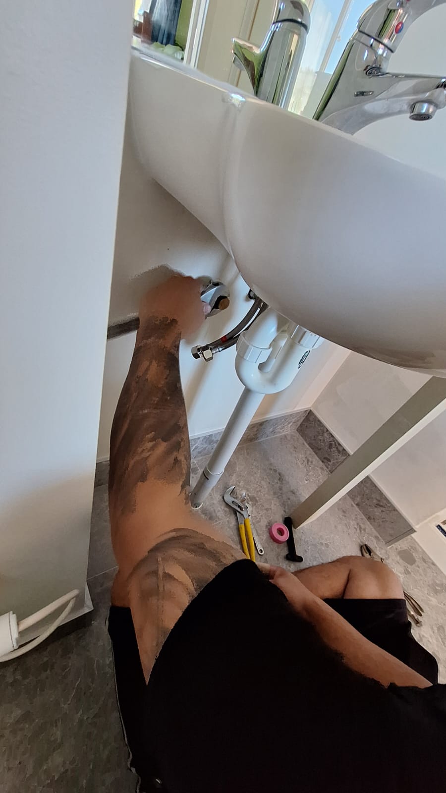 TradePlus plumber working under a bathroom basin repairing tap connections and waste pipework