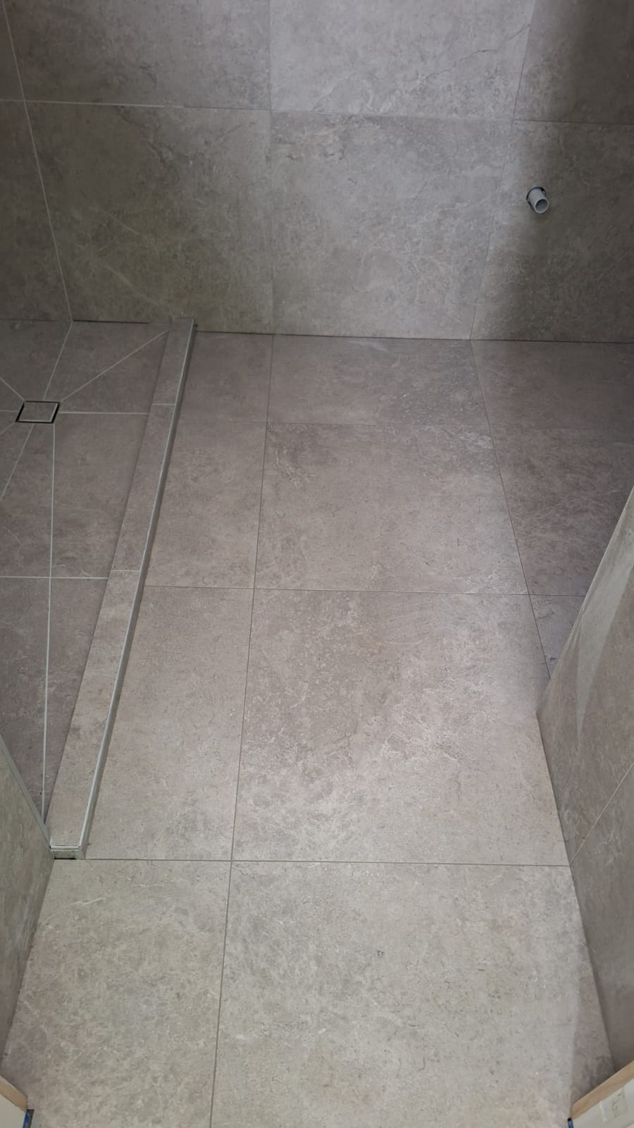 Completed large-format stone-look floor and wall tiling in an Auckland bathroom shower with linear drain and tiled step