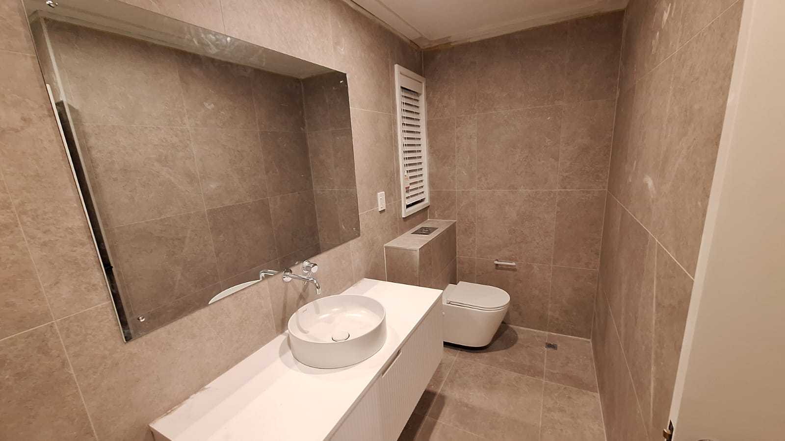 Completed TradePlus bathroom renovation in Auckland with large-format stone-look tiles, wall-hung vanity with vessel basin, frameless mirror and wall-hung toilet