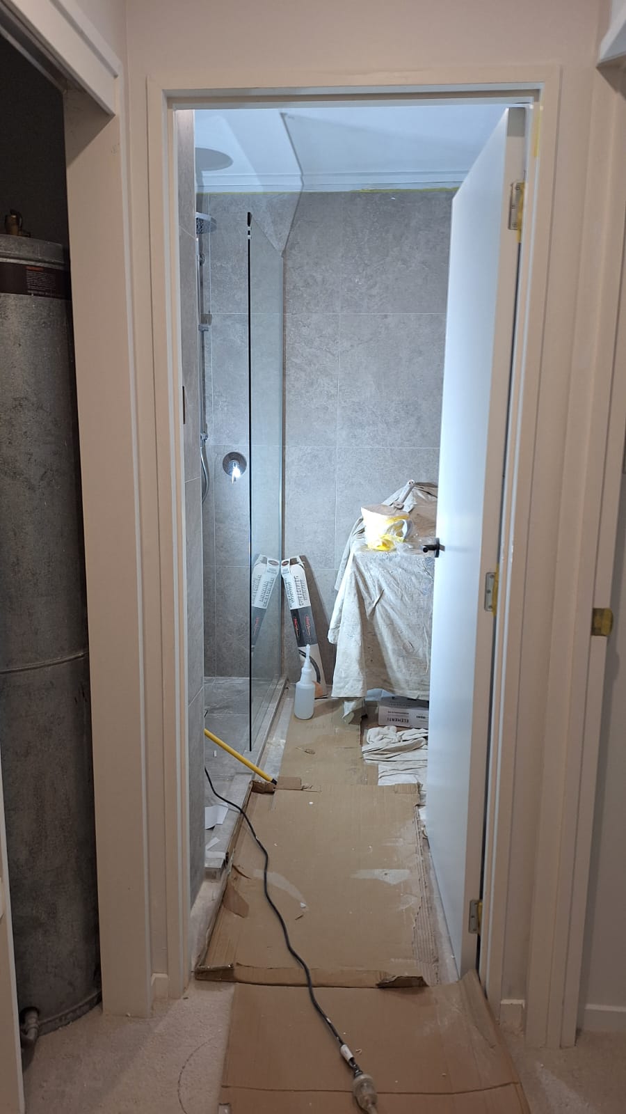 Bathroom upgrade in progress in Auckland with new grey tiled walk-in shower and frameless glass panel